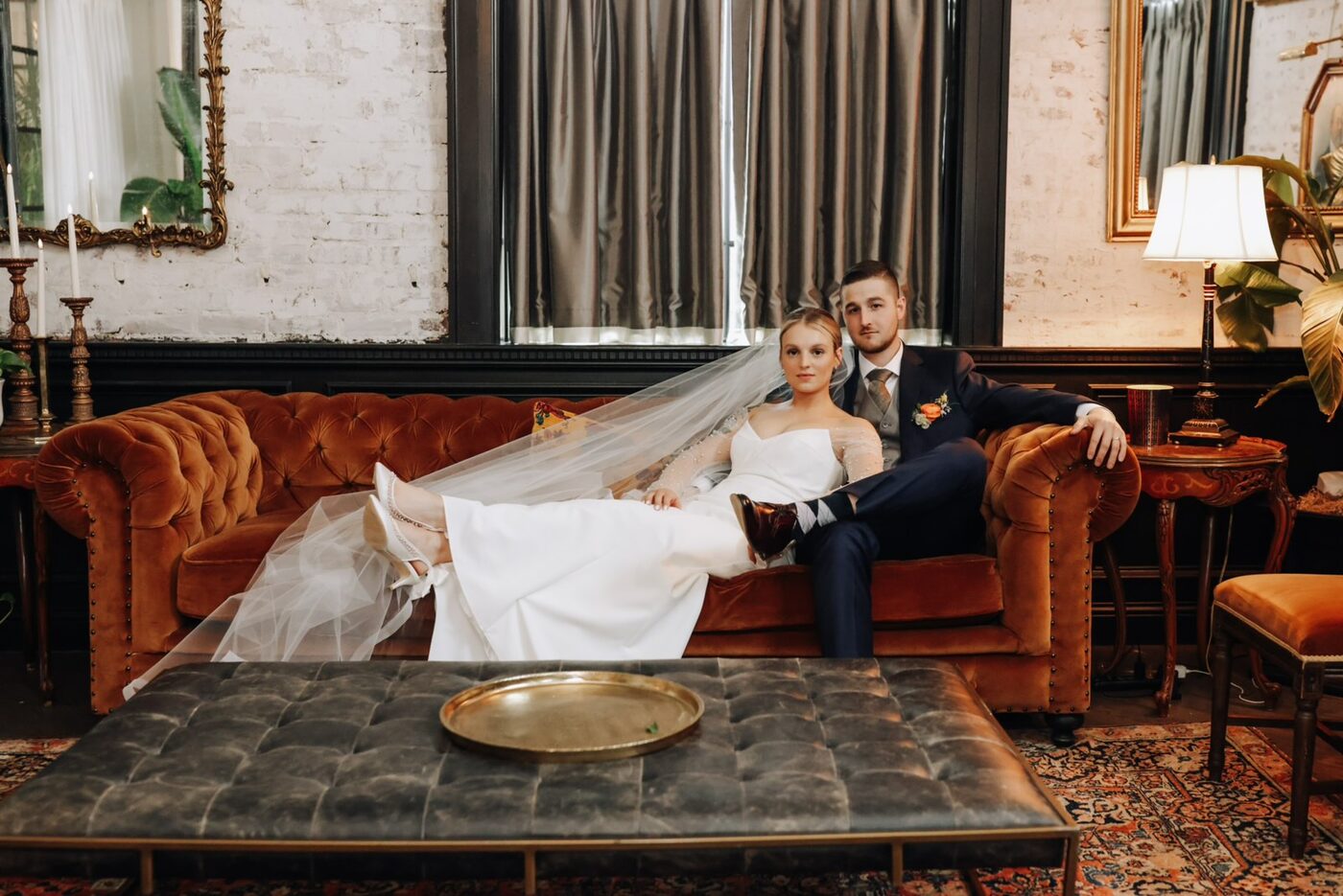 Couple seated on a velvet Chesterfield sofa, veil draped across