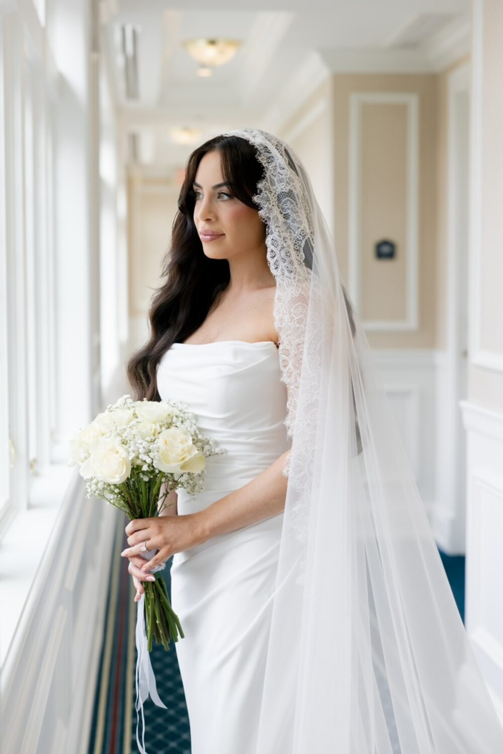 Bride in a lace-edged mantilla veil holding a white bouquet